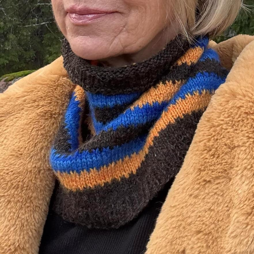 Neulottu kauluri puolittain avoimena naisen kaulassa. Kaulurin värit ovat luonnonmusta, kirkkaan sininen ja oranssi. Värit muodostavat raitoja, joiden vaihtumiskohdassa on koristeellinen kuvio kuin hammastus.