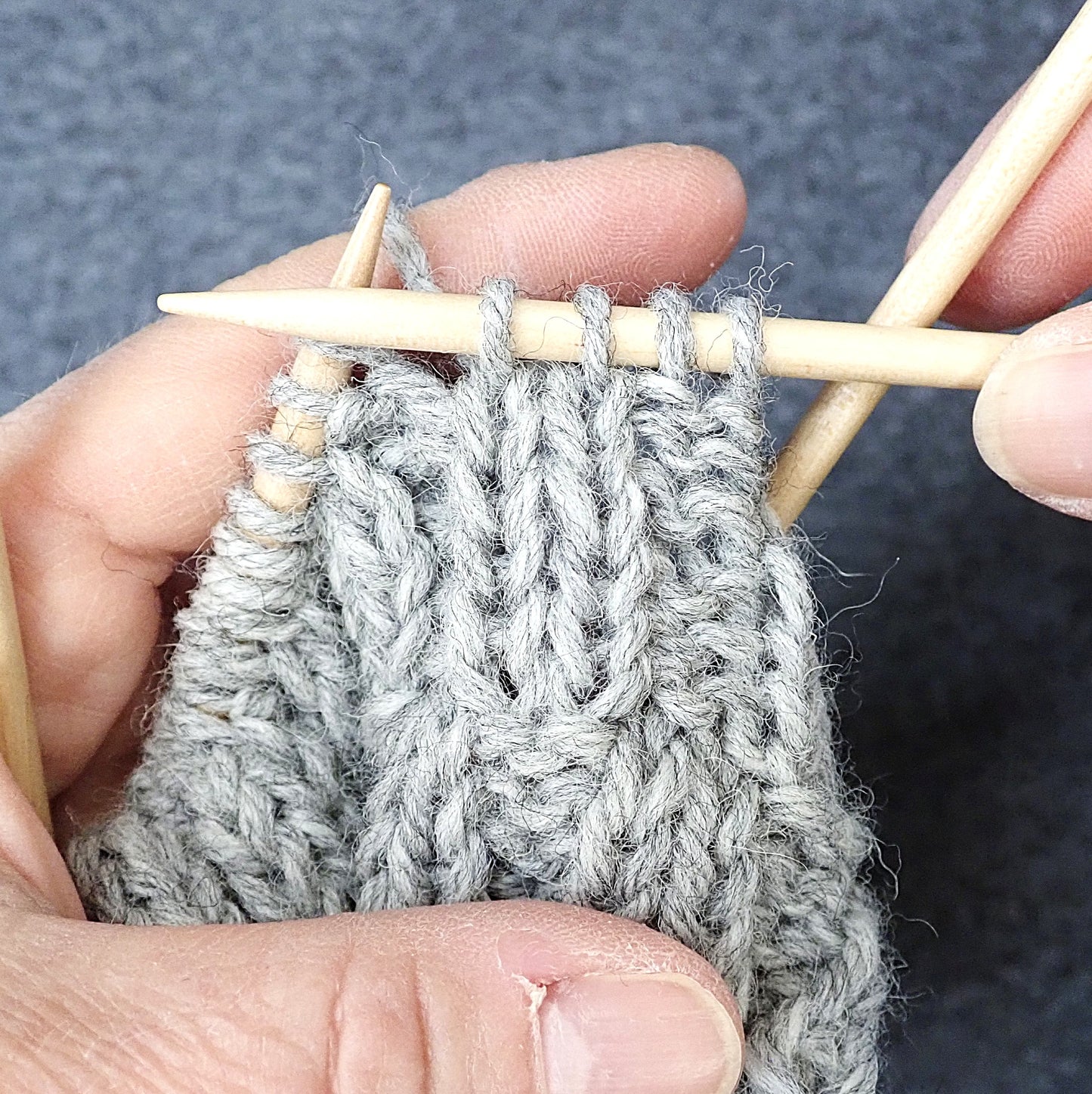 Harmaasta langasta neulotaan oikeita ja nurjia silmukoita niin, että kuvio muistuttaa korinpohjaa.