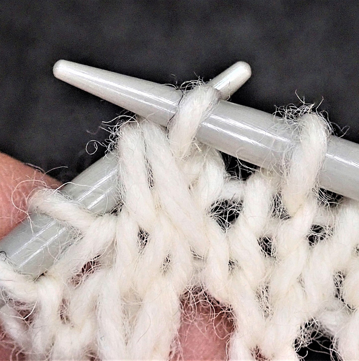 Valkoisesta langasta neulotaan pitsikuviota. Menossa on kahden silmukan neulominen yhteen takareunoistaan.