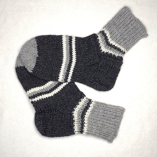 Neulotut villasukat, joissa on tummanharmaita, valkoisia ja mustia raitoja.