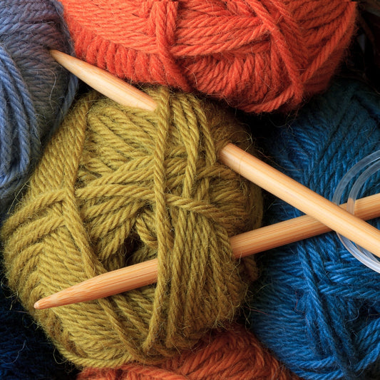 Oranssi, vihreä ja kaksi sinistä lankakerää, joihin on työnnetty ristiin puiset neulepuikot.