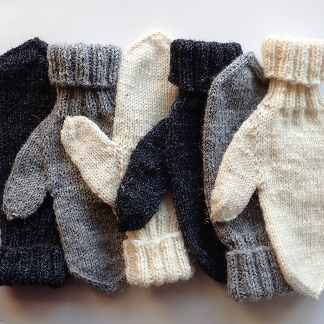 Mustia, harmaita ja luonnonvalkoisia lapasia lomittain.