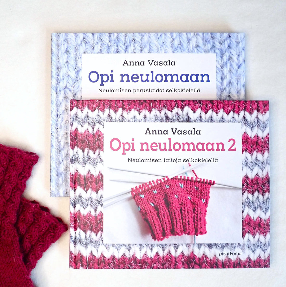Opi neulomaan -kirjat lomittain pöydällä. Vieressä palmikkovartiset, viininpunaiset lasten villasukat.