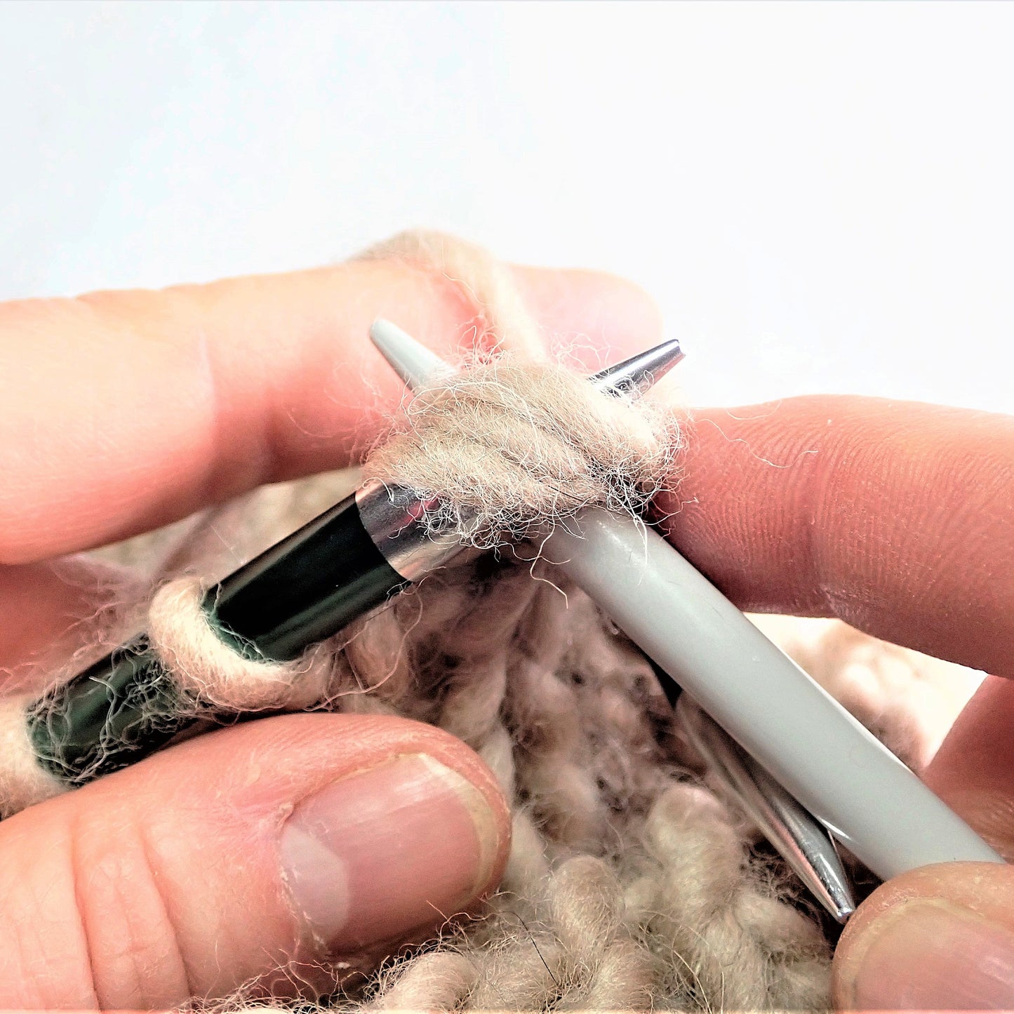 Beigeä paksua lankaa puikoilla. Kolmea silmukkaa neulotaan oikein yhteen.