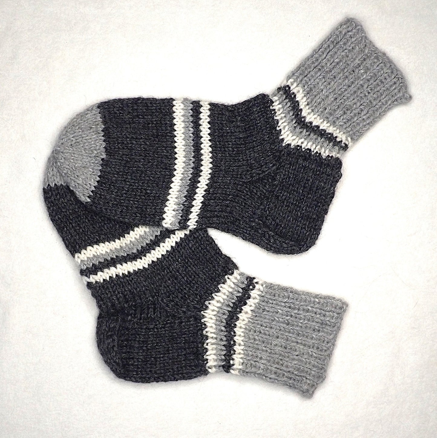 Paksut villasukat, joissa on tumman- ja vaaleanharmaita sekä luonnonvalkoisia raitoja. Helppo kantapään ohje.