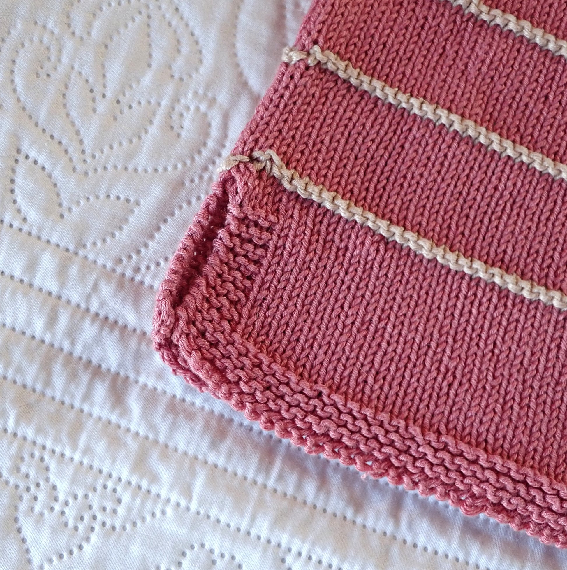 Vaaleanpunaisen neulepuseron helman sivuhalkio. Reunoja kehystää ainaoikeinneule.