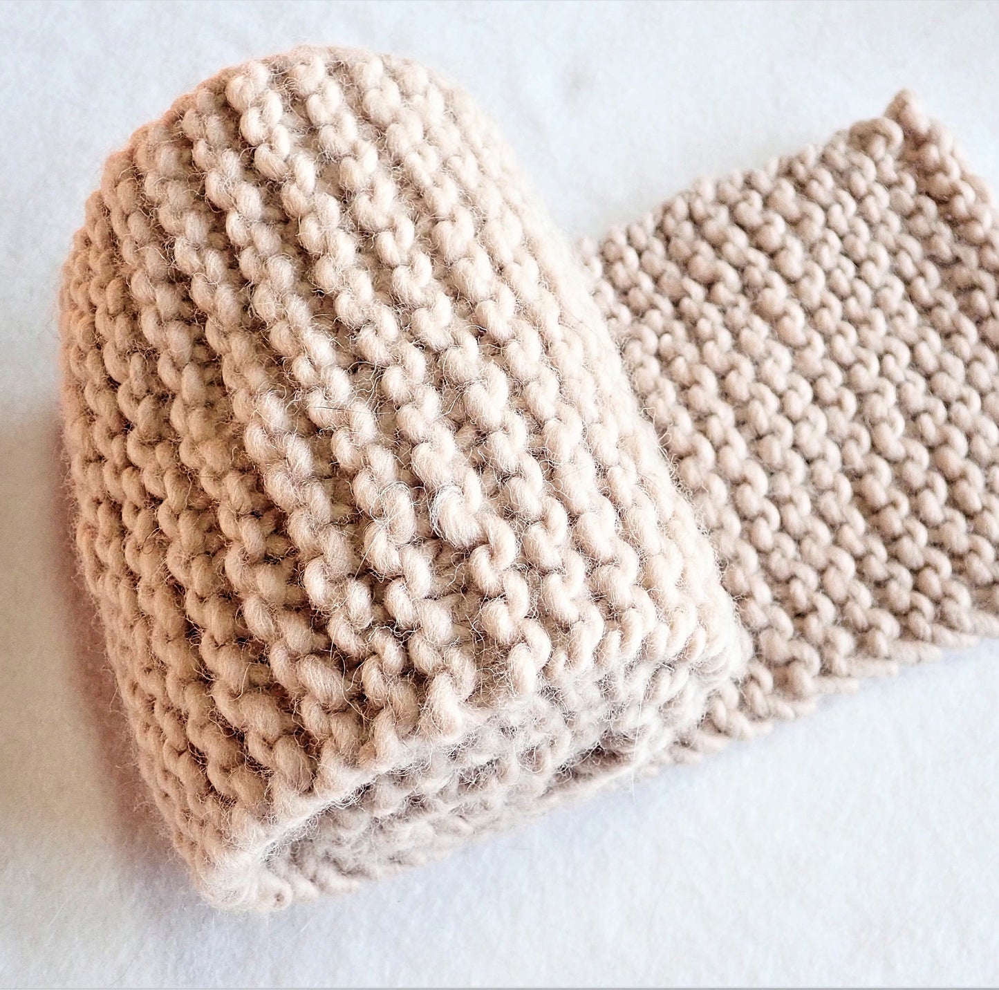 Paksu neulottu beigen värinen kaulahuivi rullalla, joka on toisesta päästään vähän auki.