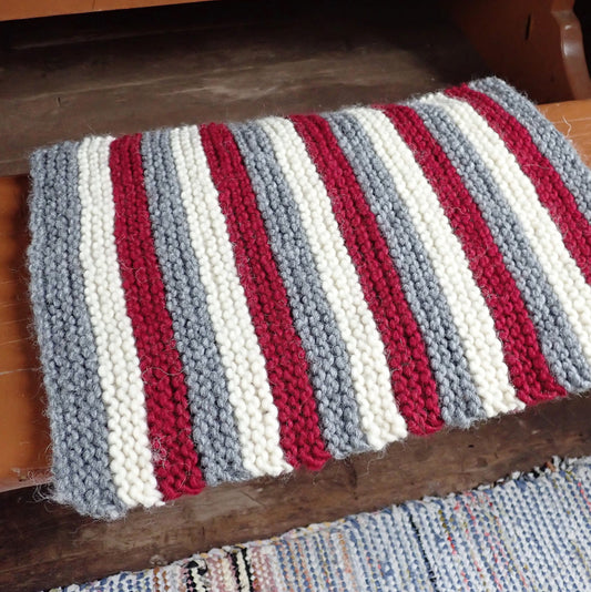 Punavalkoharmaa raidallinen istuinalusta vanhan puisen penkin päällä.