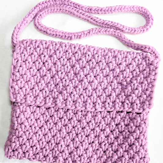 Valmis, lilan syreenin värinen olkalaukku, jossa on etuläppä. Laukun pinta on kahden kerroksen helmineuletta ja olkahihna on putkineuletta.