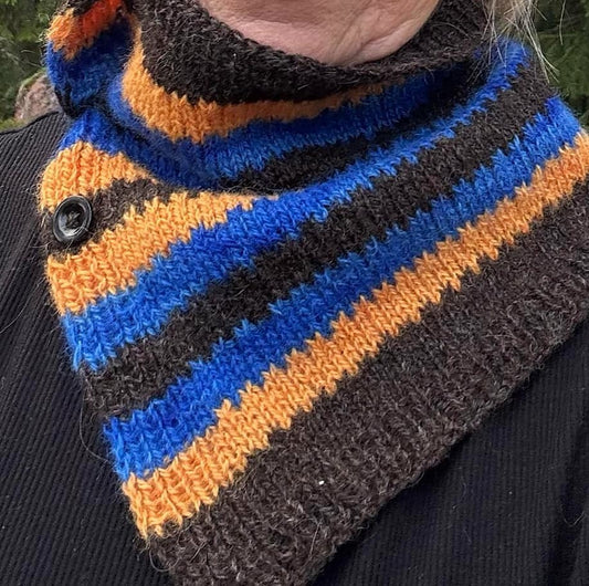 Neulottu kauluri puolittain avoimena naisen kaulassa. Kaulurin värit ovat luonnonmusta, kirkkaan sininen ja oranssi. Värit muodostavat raitoja, joiden vaihtumiskohdassa on koristeellinen kuvio kuin hammastus.