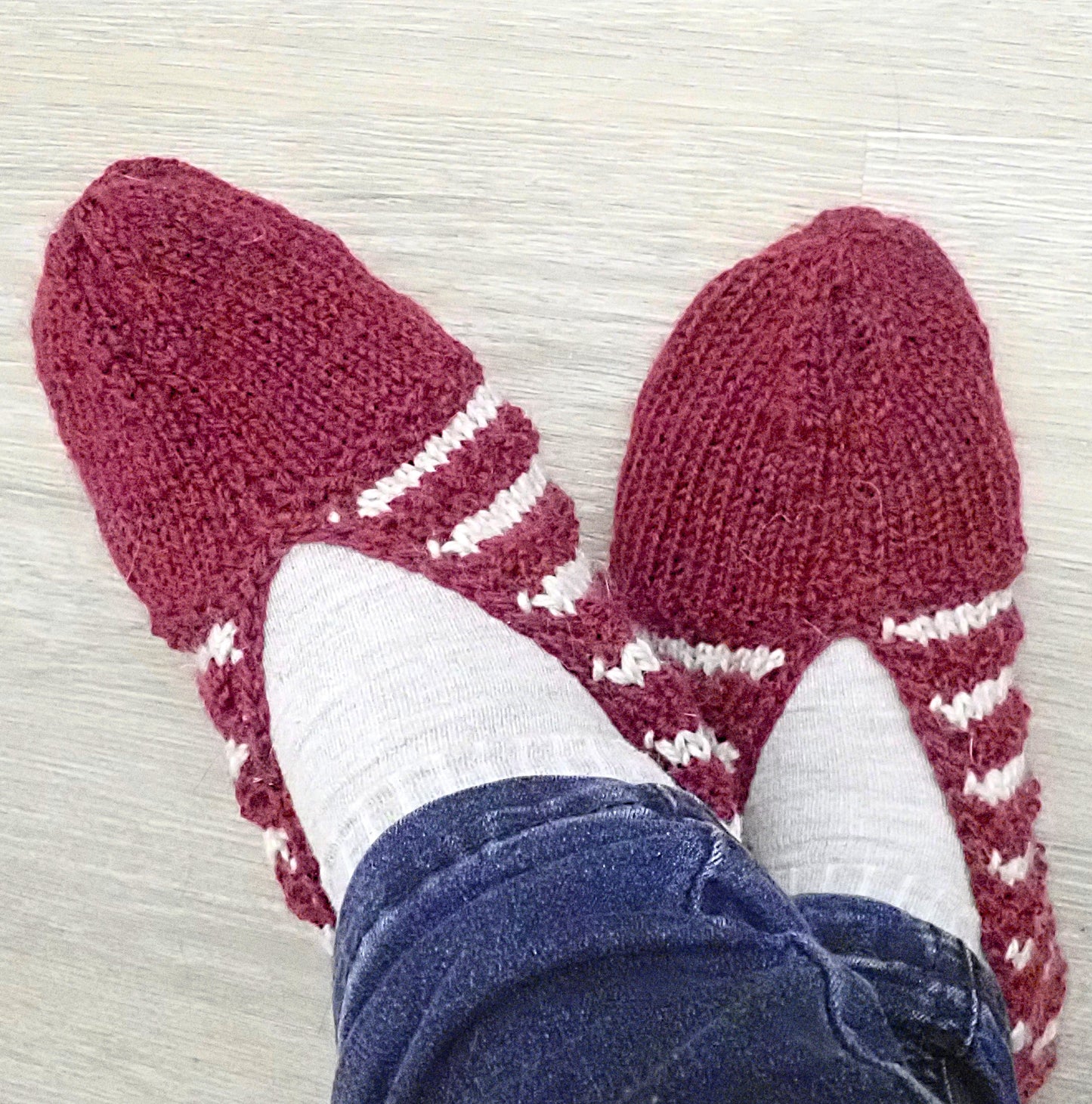 Viininpunaiset neulotut tossut, joissa on vaaleanharmaita, lähes valkoisia raitoja. Tossujen pitäjällä on farkut jalassaan.