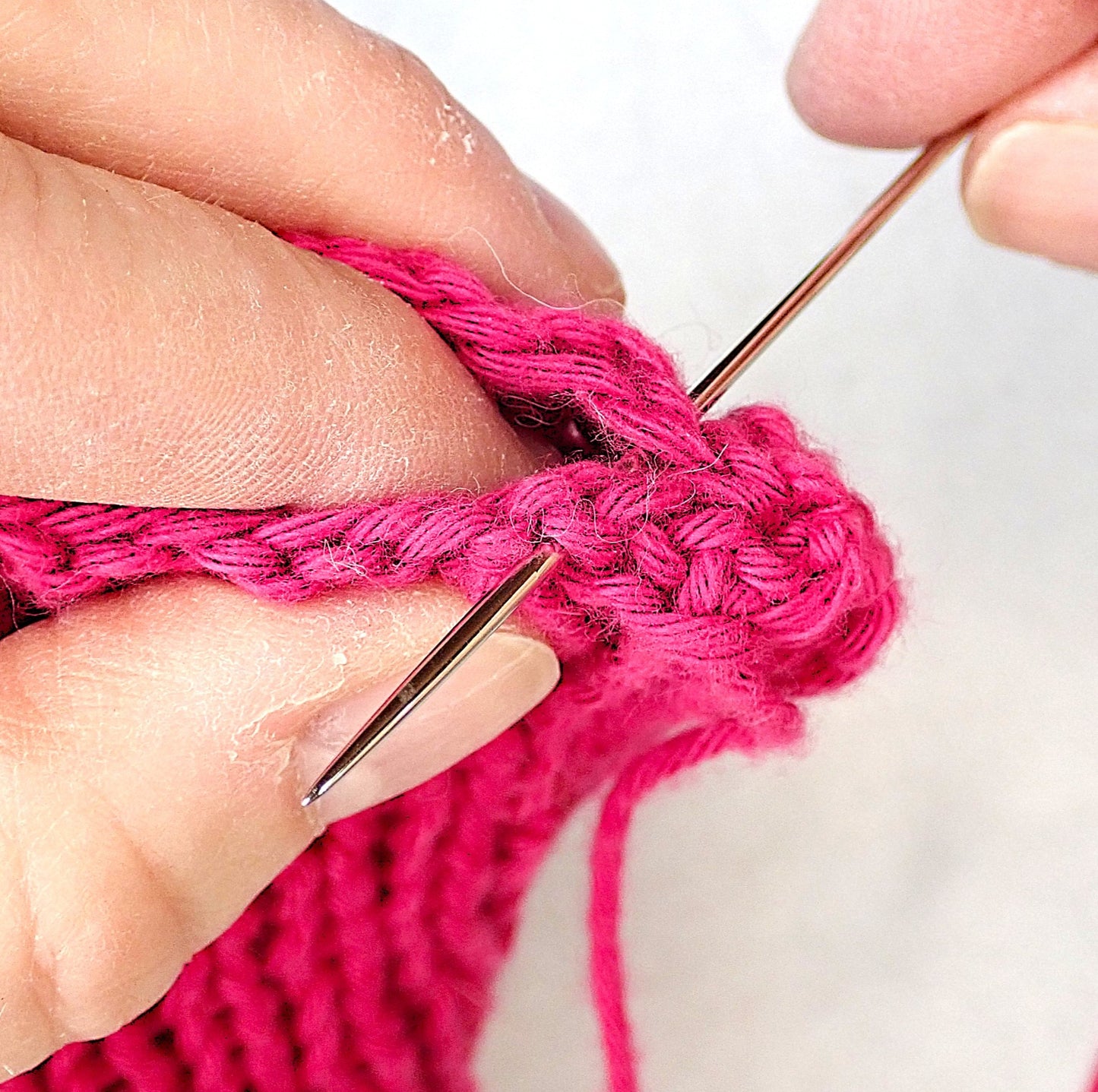 Fuksianpunaisen joustinneuleen saumaa ommellaan parsinneulan avulla.