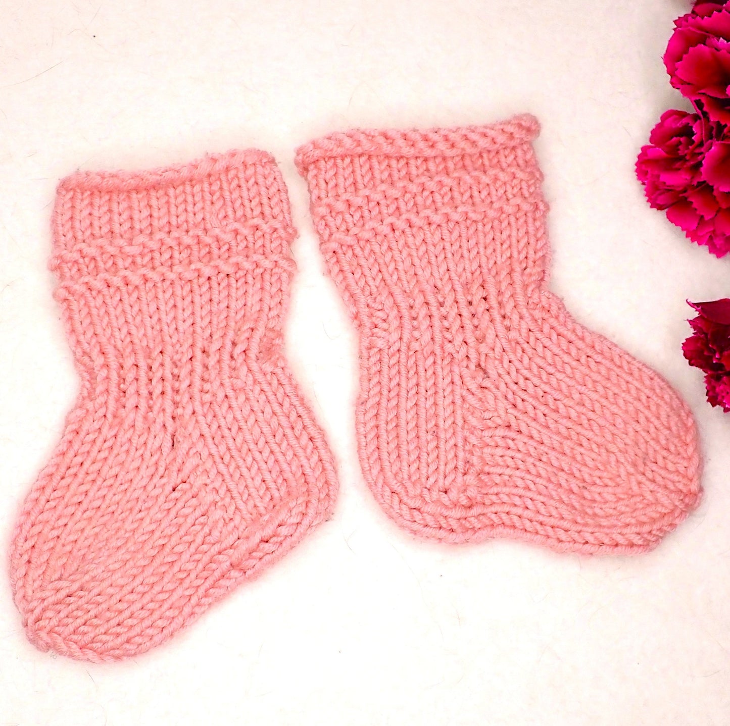 Vaaleanpunaiset vauvan sukat, joiden varressa tehosteena 2 kohoneuleraitaa.
