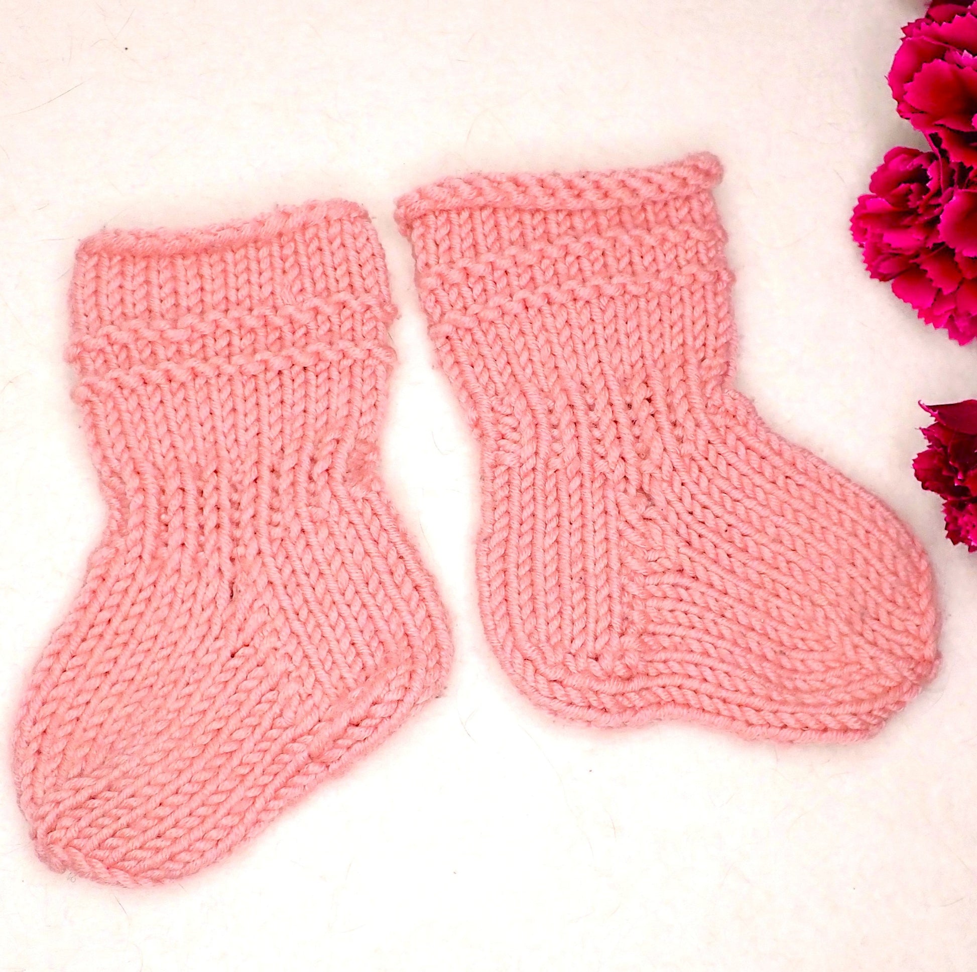 Vaaleanpunaiset vauvan sukat, joiden varressa tehosteena 2 kohoneuleraitaa.