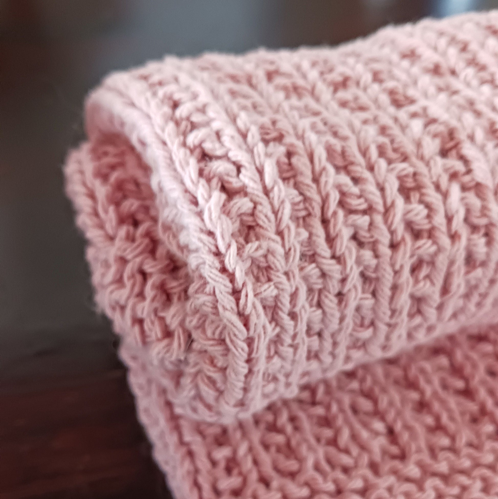 Vaaleanpunainen neulottu keittiöpyyhe rullalla tummalla puupöydällä.