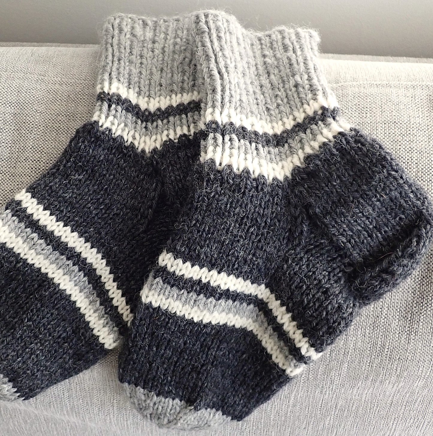 Paksut villasukat, joissa on tumman- ja vaaleanharmaita sekä luonnonvalkoisia raitoja. 