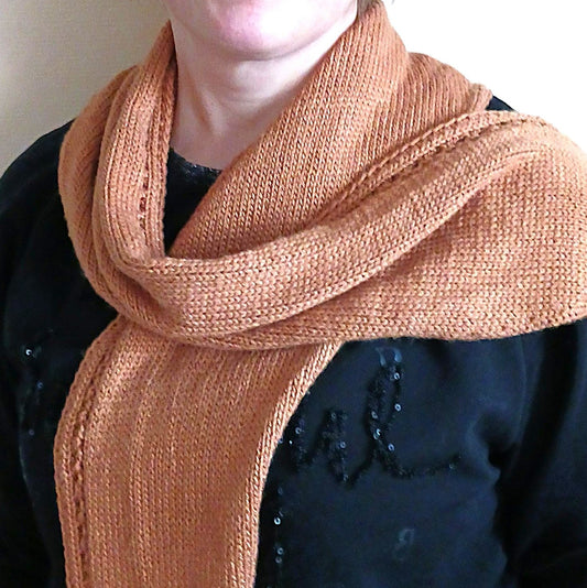 Viljankeltainen kapea kolmiohuivi on kiedottu löysästi naisen kaulaan. Huivin yläreunassa on pitsineuleraita.