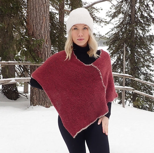 Nuori vaaleahiuksinen nainen seisoo ulkona lumisen maiseman edessä. Hänellä on yllään musta paita ja legginssit, viininpunainen neulottu poncho ja päässä valkoinen pipo.