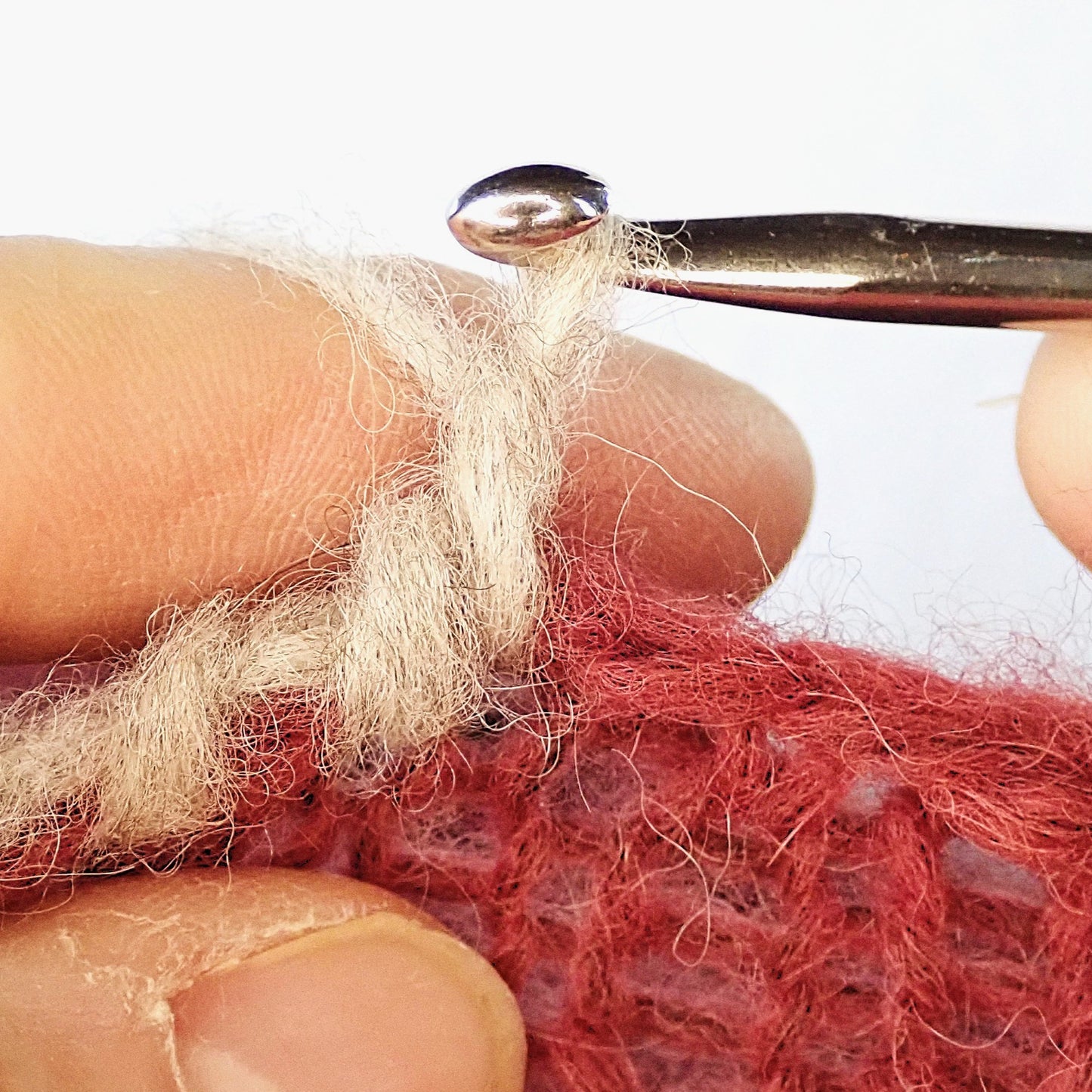 Rapuvirkkaus beigestä pörrölangasta punaisen neuleen reunaan.