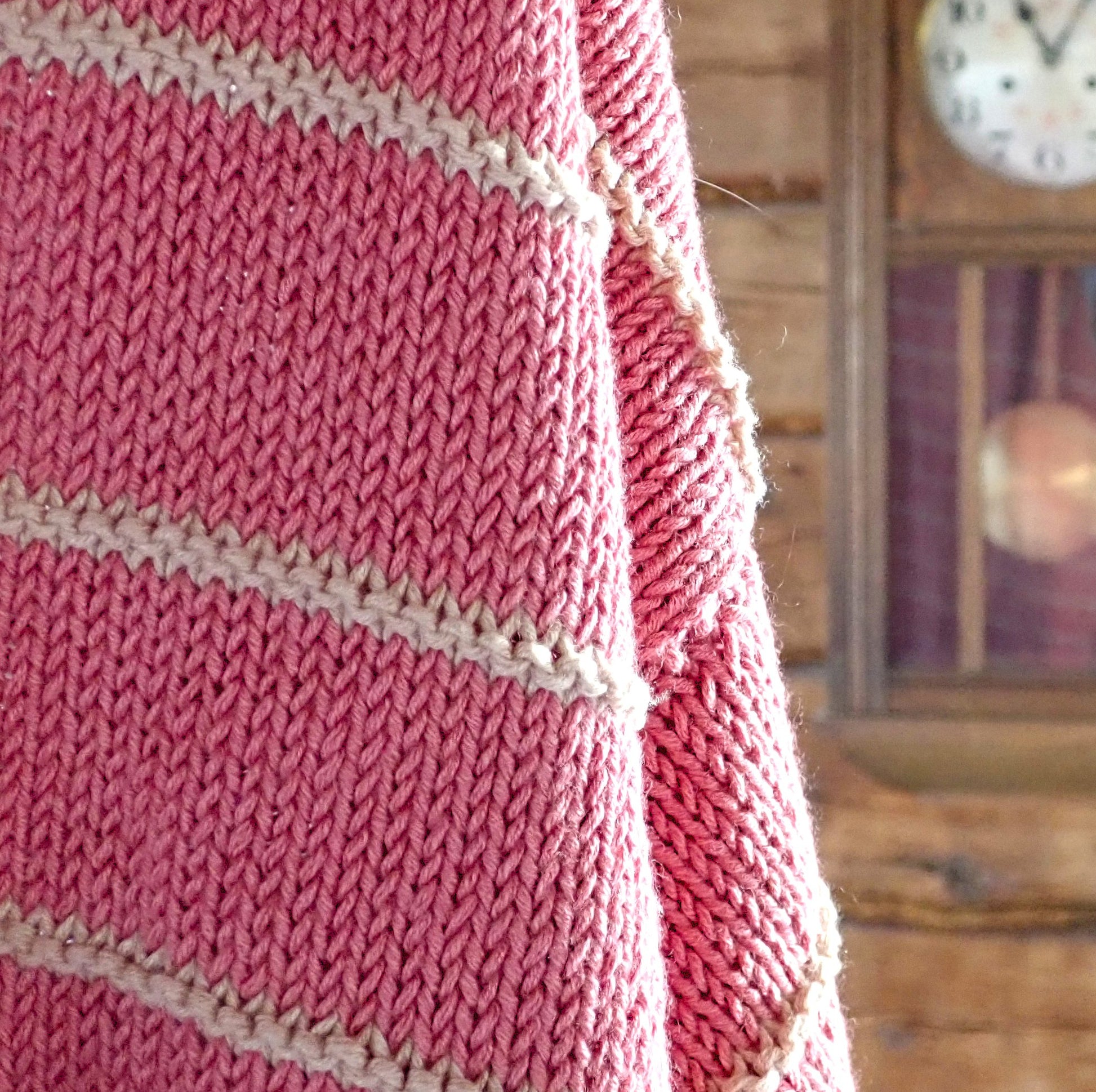 Osa Kesäpäivä-neulepuserosta näkyvillä. Taustalla häämöttää hirsiseinä ja vanha seinäkello.