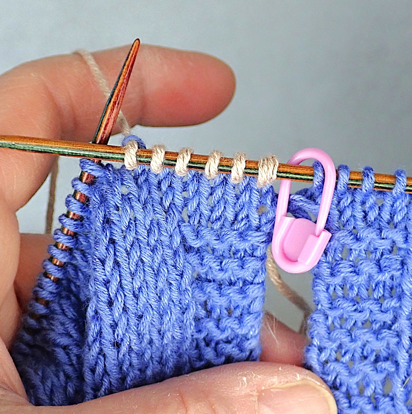 Taivaansiniseen puseroon on alettu neulomaan beigeä raitaa. Vaaleanpunainen silmukkamerkki näyttää puseron sivusauman paikan.