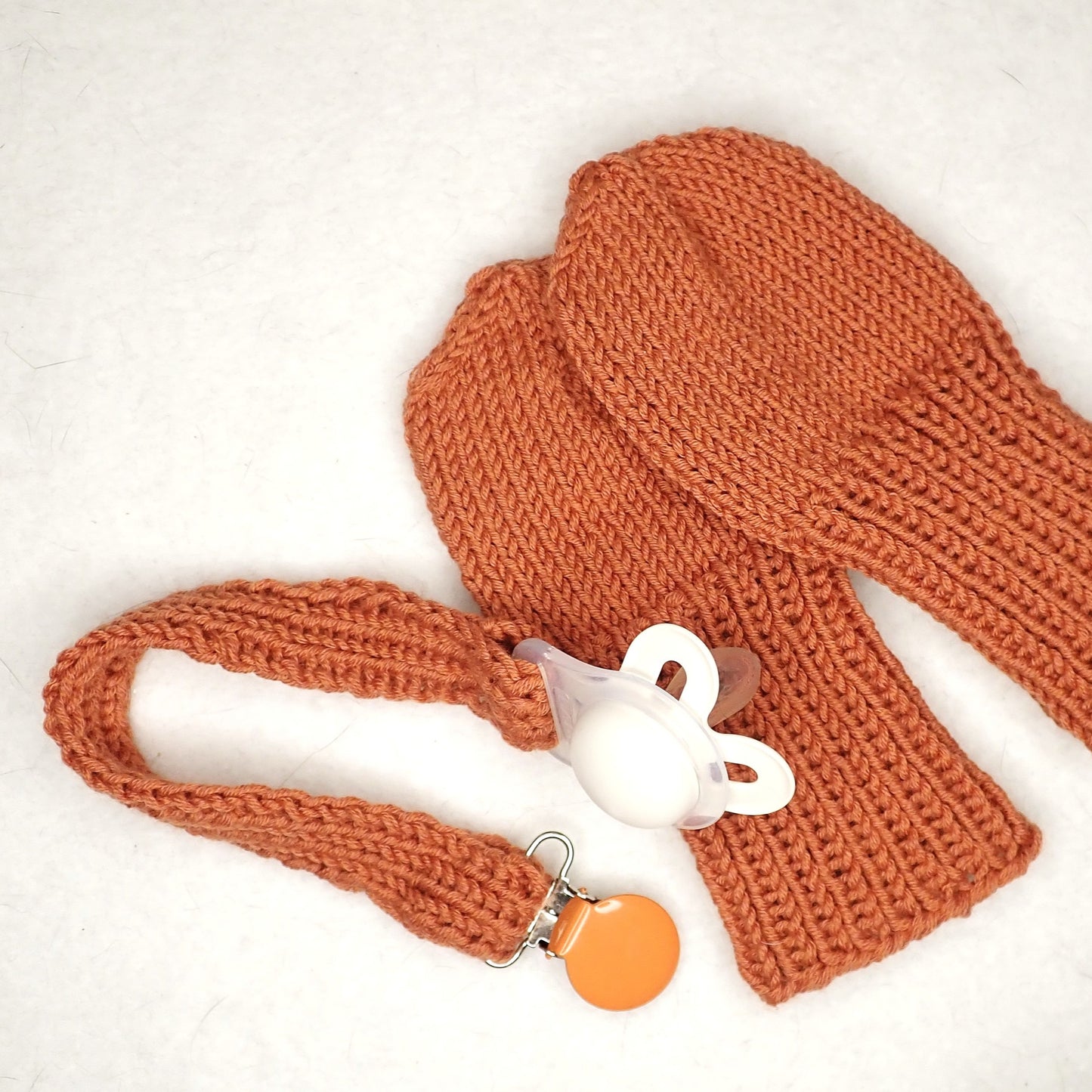 Oranssit neulotut vauvan tumput ja tuttinauha. 