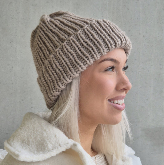 Hymyilevä nuori nainen, jolla on päässään muhkea beige joustinneulepipo.