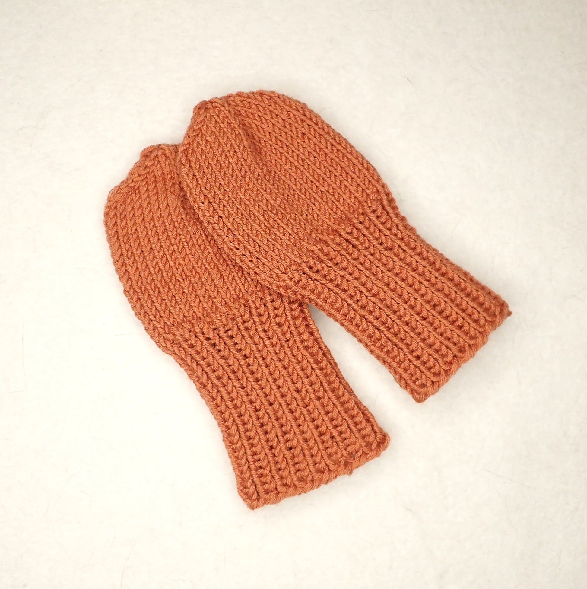 Oranssista langasta neulotut helpot vauvan lapaset.