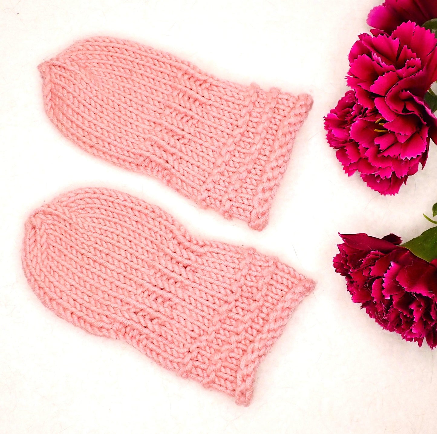 Vaaleanpunaiset vauvan lapaset, joiden vieressä on kolme viininpunaista neilikkaa. 