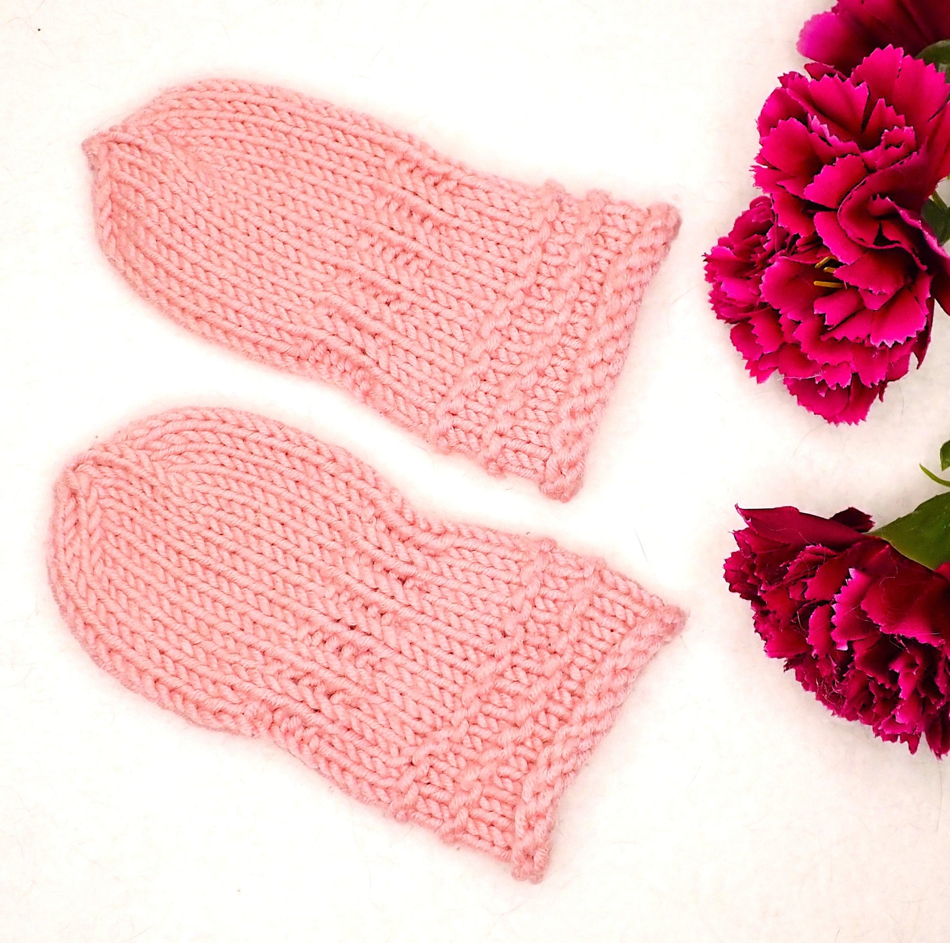 Vaaleanpunaiset vauvan lapaset, joiden vieressä on kolme viininpunaista neilikkaa. 